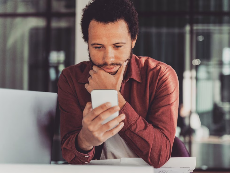 Homme concentré consultant son smartphone dans un environnement de bureau moderne
